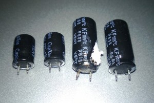 The 220 µF capacitors on the left have noticeable wavy cases from internal pressure buildup, while the 1000 µF capacitor in the middle has actually blown its plug out of the bottom of its case.